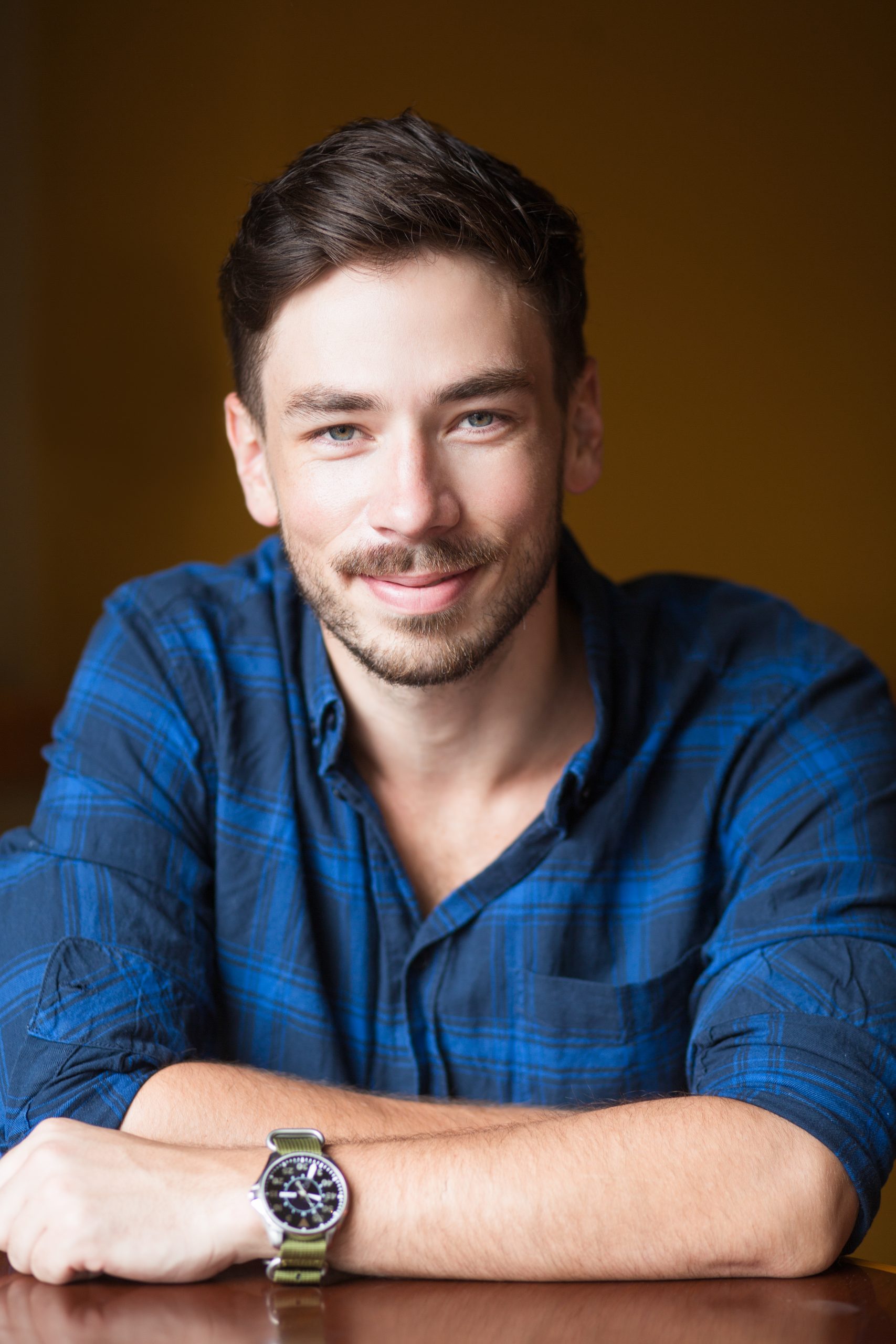 Closeup portrait of smiling young handsome man looking at camera and sitting at empty table. Front view.